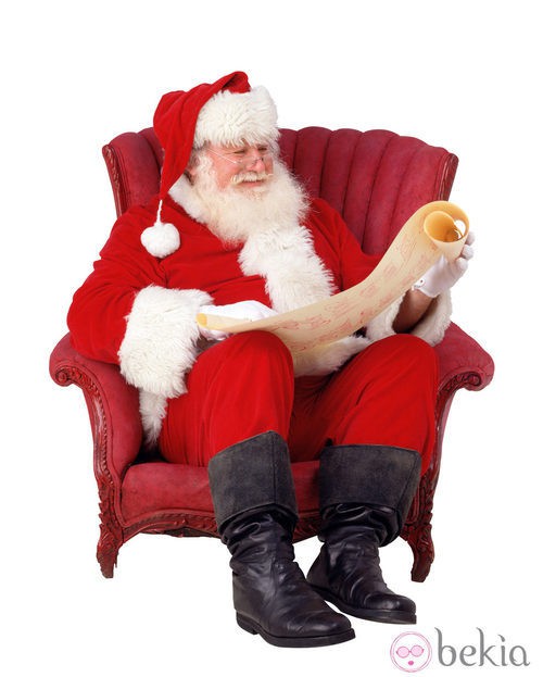 Papá Noel lee la carta de los regalos sentado en un sillón